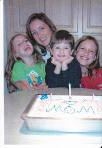 mom and three small children smiling with cake on table