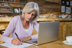 woman filling out worksheet with computer in kitchen