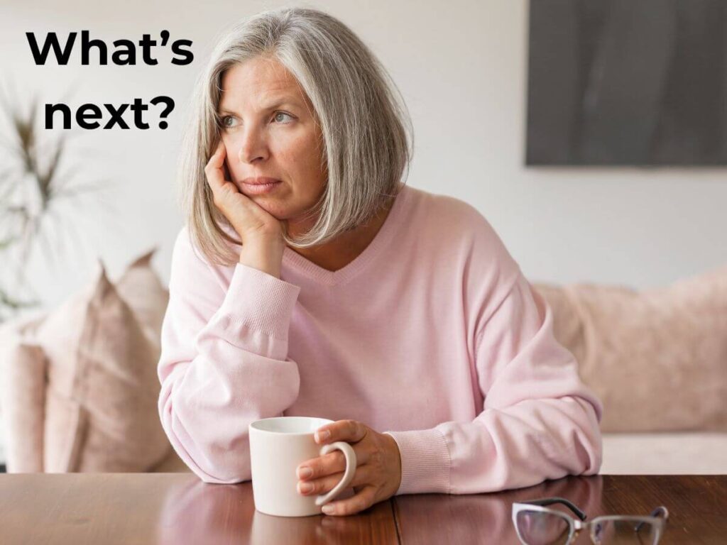 middle-aged empty nester mom sitting alone at kitchen table with cup of coffee asking herself what's next after kids moved out